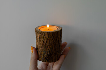 Wooden log candle holder in woman’s hand on plain background