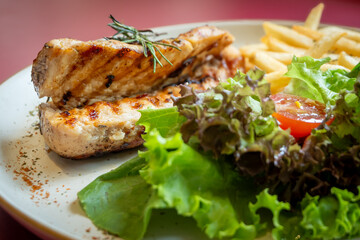 Close-up of grilled chicken breast garnished with rosemary, served with french fries and fresh salad, showcasing a delicious and healthy meal