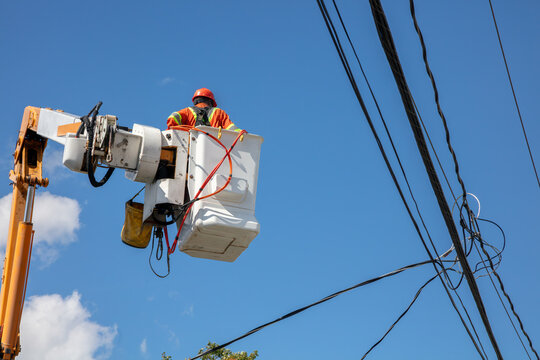 Electrical lineman in bucket truck working on power lines against blue sky