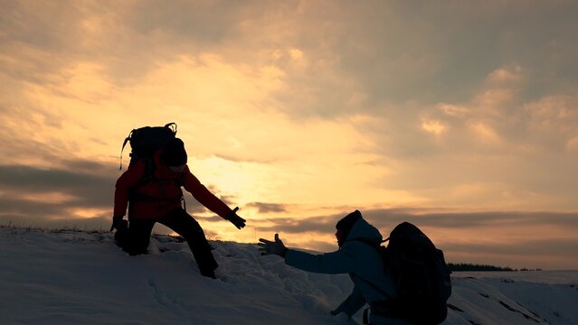 Teamwork of business people. Go to your goal. Travelers climb snowy mountain together. Silhouettes of climbers reaching out to each other, climbing to top of the hill. Victory of business team. Travel - Powered by Adobe