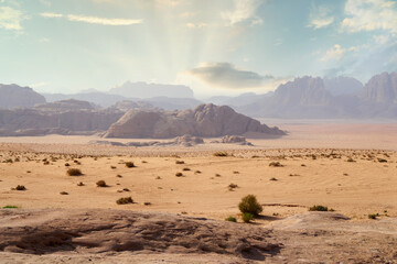 Desert landscape with mountains and sun rays in background during daytime hours. Wadi Rum, Jordan.