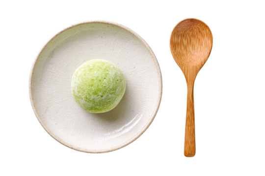 Light green, orb-shaped ice cream on a light beige plate, beside a wooden spoon