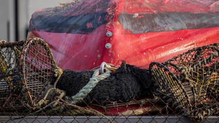 Crab pots on quayside with hull of small red boat in the background