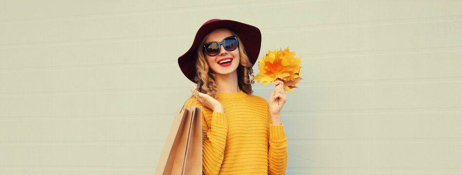 Autumn portrait of beautiful happy woman with shopping bag, stylish girl holding yellow leaves