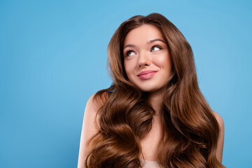 Beautiful lovely woman with long wavy brown hair and natural makeup posing against a blue background