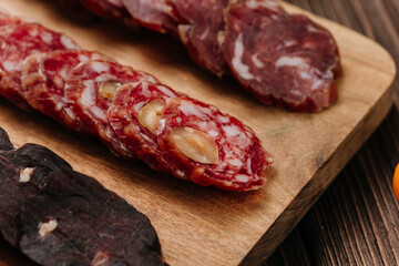Close-up of gourmet sliced sausage with nuts on wooden board, traditional cured meat snack