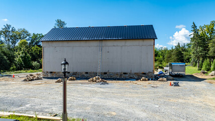 Work is underway on a large barn in a rural location. A ladder leans against the structure while...