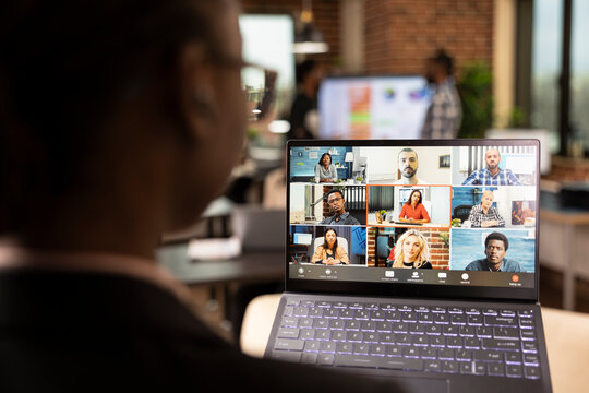 Rearview closeup of black businesswoman attending videoconference call with multiethnic colleagues working remotely. The focus is selectively on laptop screen displaying an ongoing virtual meeting. - Powered by Adobe