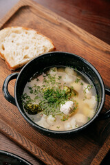 Clear soup with vegetables and chicken meatballs, served with rustic bread on wooden tray