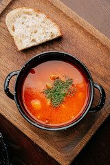 Traditional red soup with herbs served with rustic bread on wooden tray, top view