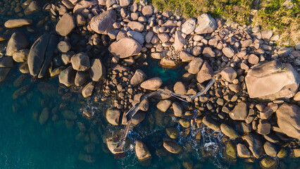 Aerial view of rocky shore with wooden walkway and turquoise ocean in Brazil