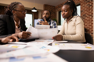 African american entrepreneurs with documents discussing and consulting around meeting table in...