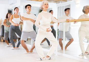 Naklejka premium Slender elderly woman doing choreography at ballet barre during gym classes