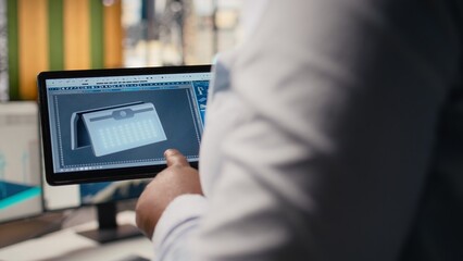 Close up of technician using tablet to create solar powered device design with alternative energy...