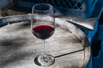 Red wine in a glass on a rustic wooden barrel under sunlight