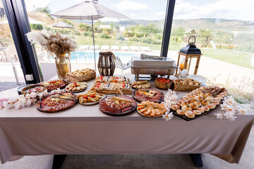 Buffet table setup with diverse appetizers and desserts beside a pool in a scenic outdoor venue