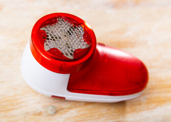 Red and white plastic handheld fabric shaver, machine for removing fabric pills from garments, closeup view on wooden background