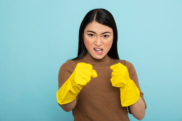 Asian housekeeper wearing yellow rubber gloves clenches fists in frustration, looking angrily at...