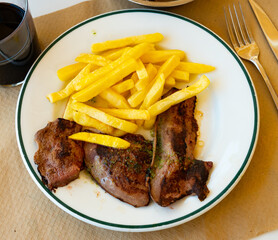 Pieces of fried lamb liver, cooked with garlic and parsley, are laid out on plate. Dish is served with side dish - portion of French fries