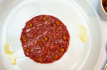 Elegant beef tartare topped with drops of yolk sauce, artfully presented with olive oil drizzle on white plate..