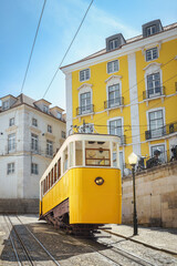Historic Portuguese funicular railway with traditional yellow car ascending hill past colorful buildings in Lisbon's Bairro Alto neighborhood, Portugal.