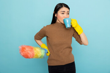 Asian female housekeeper holds a duster and enjoys coffee during spring cleaning. Pretty asian...