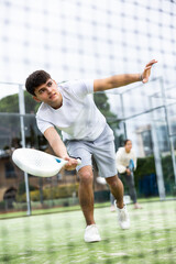 Sportive young man playing padel together with a partner. View through the tennis net