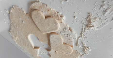 Close-up of raw dough on a floured surface with heart-shaped cutouts, ready for baking cookies or pastries, symbolizing homemade cooking, love, and celebration.