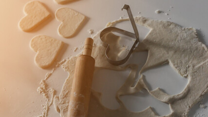 Heart-shaped cookies cut from rolled dough with a metal cutter and wooden rolling pin on a floured surface, symbolizing homemade baking and festive preparation.