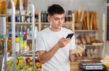 Positive guy purchaser scanning QR code or barcode of dried meat in supermarket