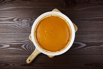 Delicious pumpkin pie in a white ceramic dish on a wooden cutting board, showcasing a smooth...