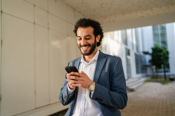 Smiling businessman using smart phone in modern office corridor