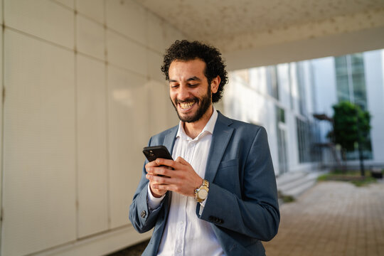 Smiling businessman using smart phone in modern office corridor