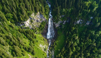 Aerial view of a waterfall cascading down a mountain valley, surrounded by dense forest