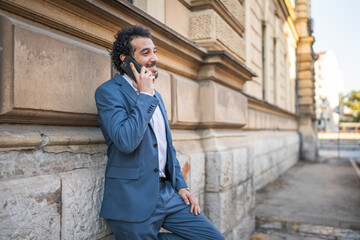 Obraz premium Elegant businessman talking on the phone and smiling near a wall