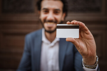 Smiling businessman showing credit card in front of wooden door