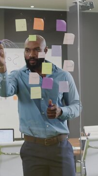 Vertical video: Surveying sticky notes, African American man sketching diagram on glass in office