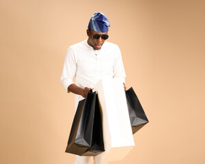 An African man wearing a white traditional outfit, blue fila cap, and sunglasses holds multiple...