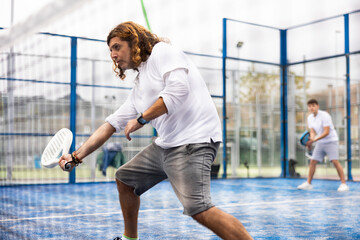 Athletic man plays padel. View through the tennis net