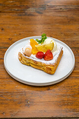 Delicious dessert with fresh fruit, ice cream, and powdered sugar on a wooden table setting