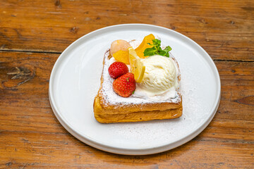 Delicious French toast with fresh fruit, ice cream, and mint on a white plate setting