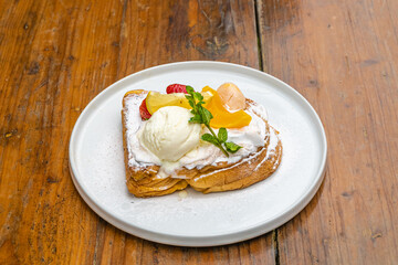 Delicious French toast dessert with fresh fruit, cream, and ice cream on wooden table