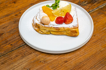 Delicious gourmet French toast dessert with fresh fruit, cream, and powdered sugar on a plate