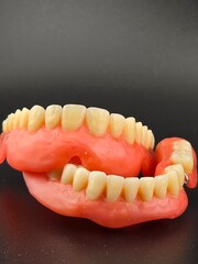A detailed studio shot of two dentures in wax on a black background, with visible pink gum material and rows of yellow-white teeth.