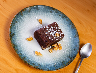 Piece of soft sweet chocolate pie brownie with walnuts sprinkled with powdered sugar. Homemade bakery and dessert..