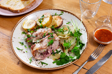 Appetizing roast leg of lamb served on plate with potatoes and onions