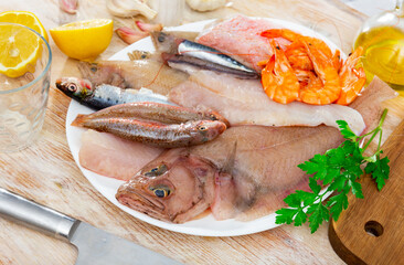 Mix of raw fish and shrimp served on plate with herbs and lemon