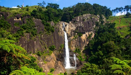 A powerful waterfall cascades down a dramatic cliff face, surrounded by lush, green tropical foliage.