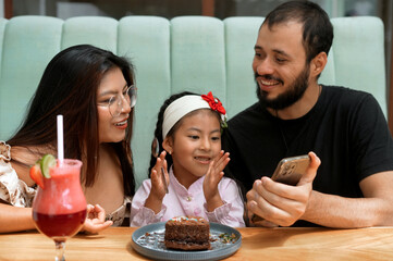 Happy family celebrating birthday with video call at restaurant