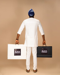 African man in white traditional attire and blue cap seen from behind, holding Black Friday...